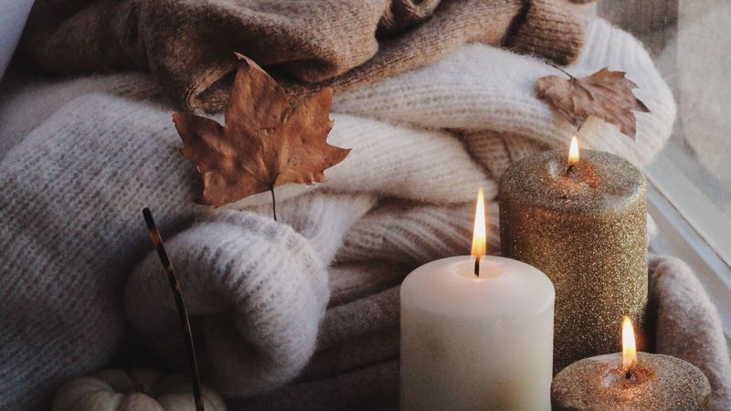 Fall vignette with lit candles, cozy blankets and autumn leaves